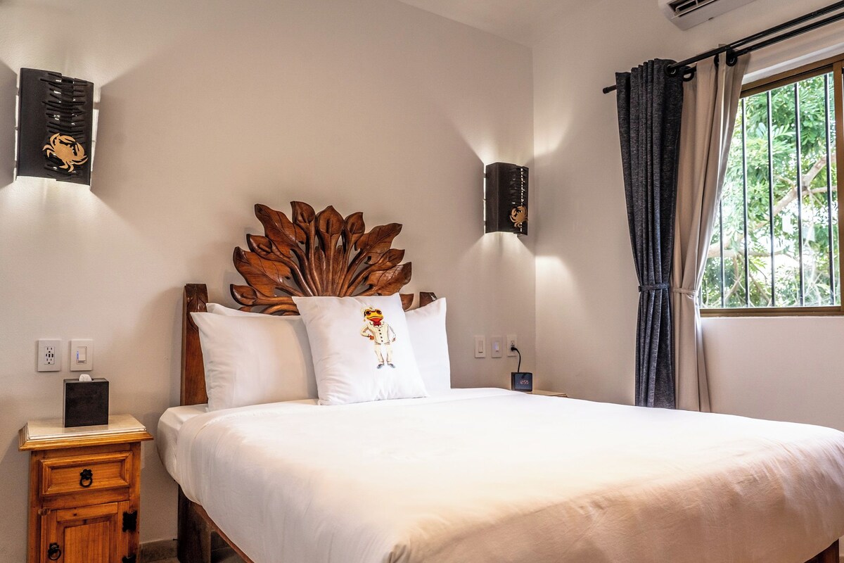 A neatly made bed with a wooden headboard, a bedside table with a lamp, and a wall-mounted light fixture.