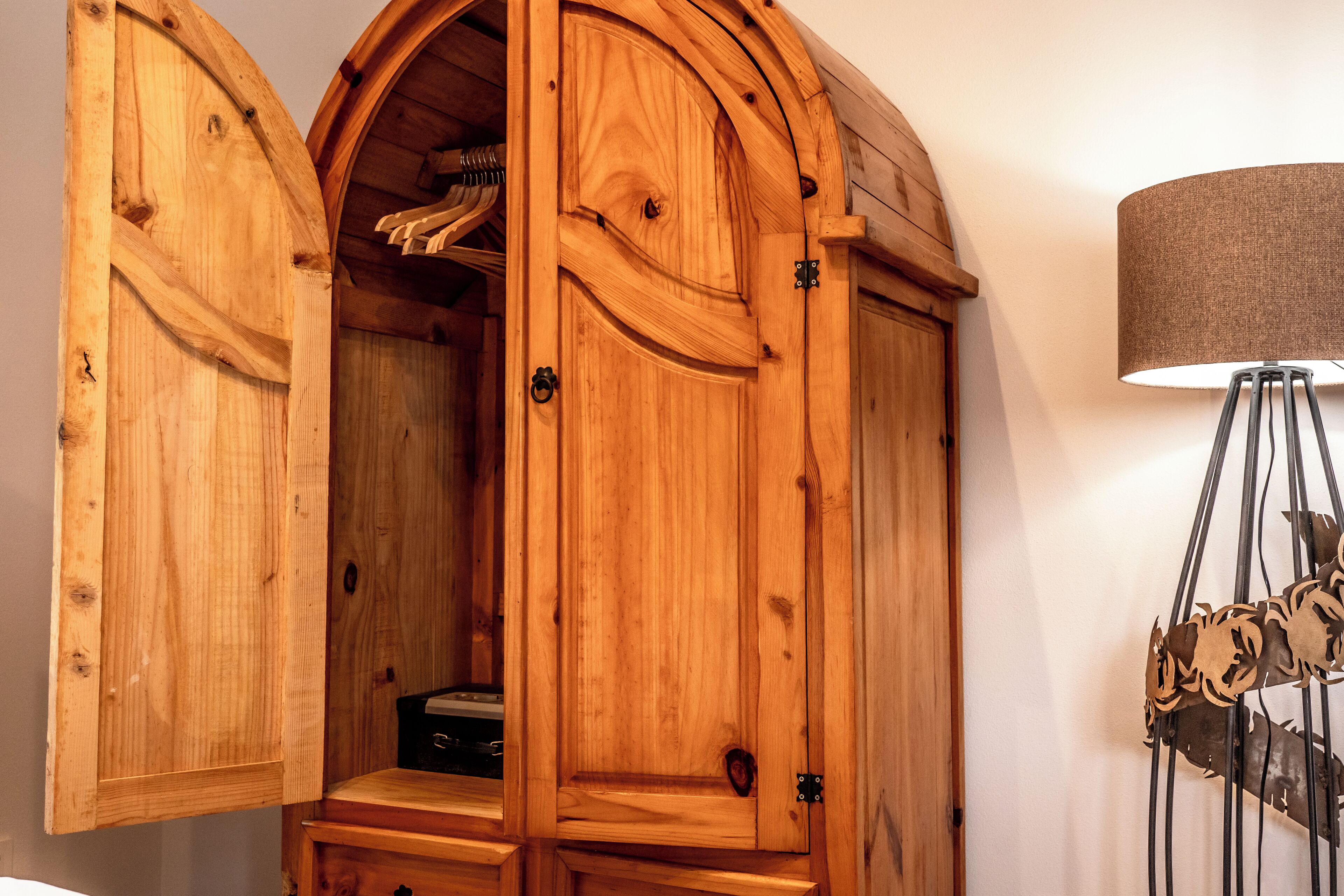 Ein hölzerner Bogenwandschrank mit Spiegel und Lampe daneben.