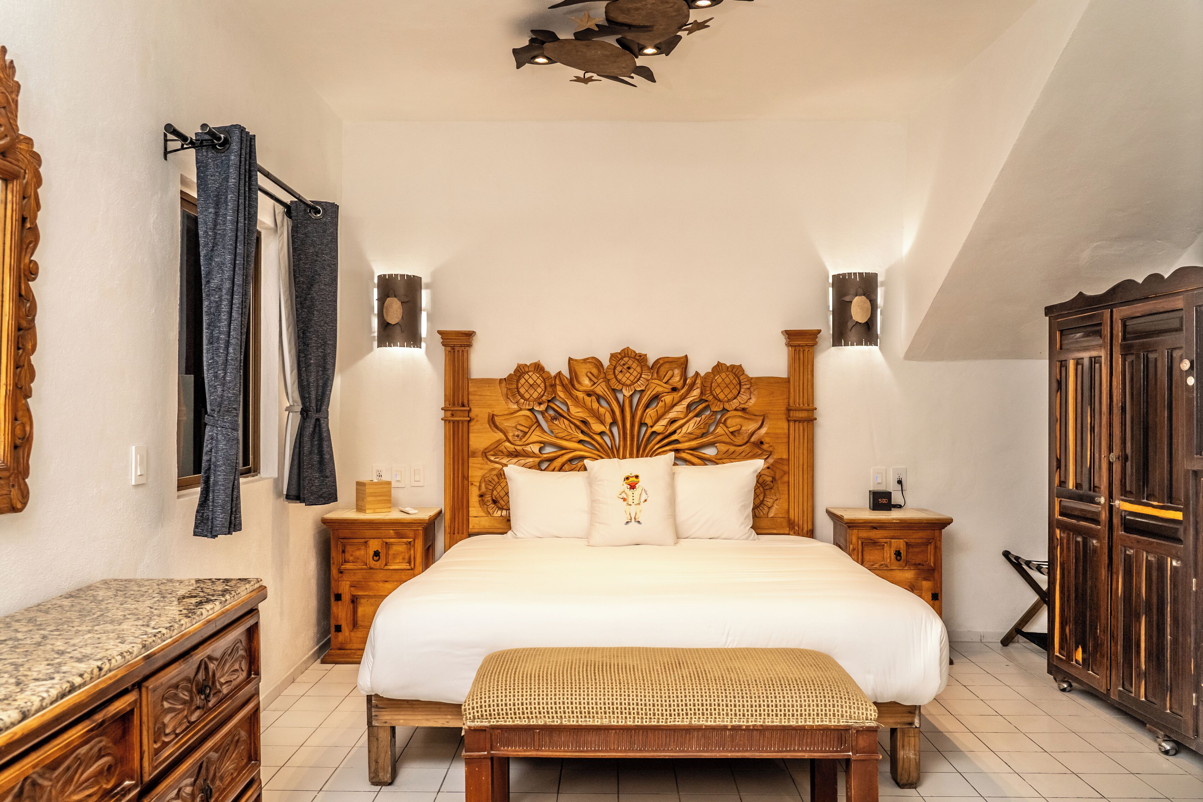A bedroom with a wooden headboard, a large bed, a bedside table, a bench, and a wardrobe.