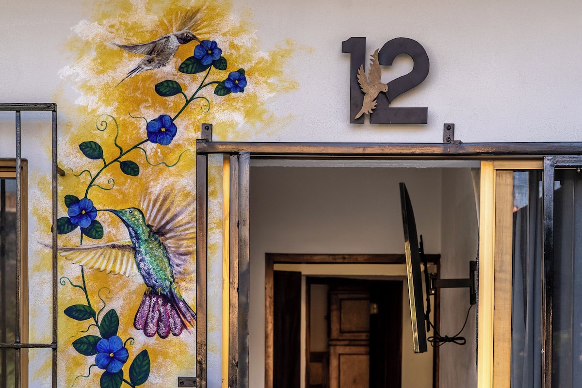 Ein Flur mit einem Schild mit der Nummer 12, einer Tür mit Fensterteil und einer Wand mit Wandgemälde von Vögeln und Blumen.