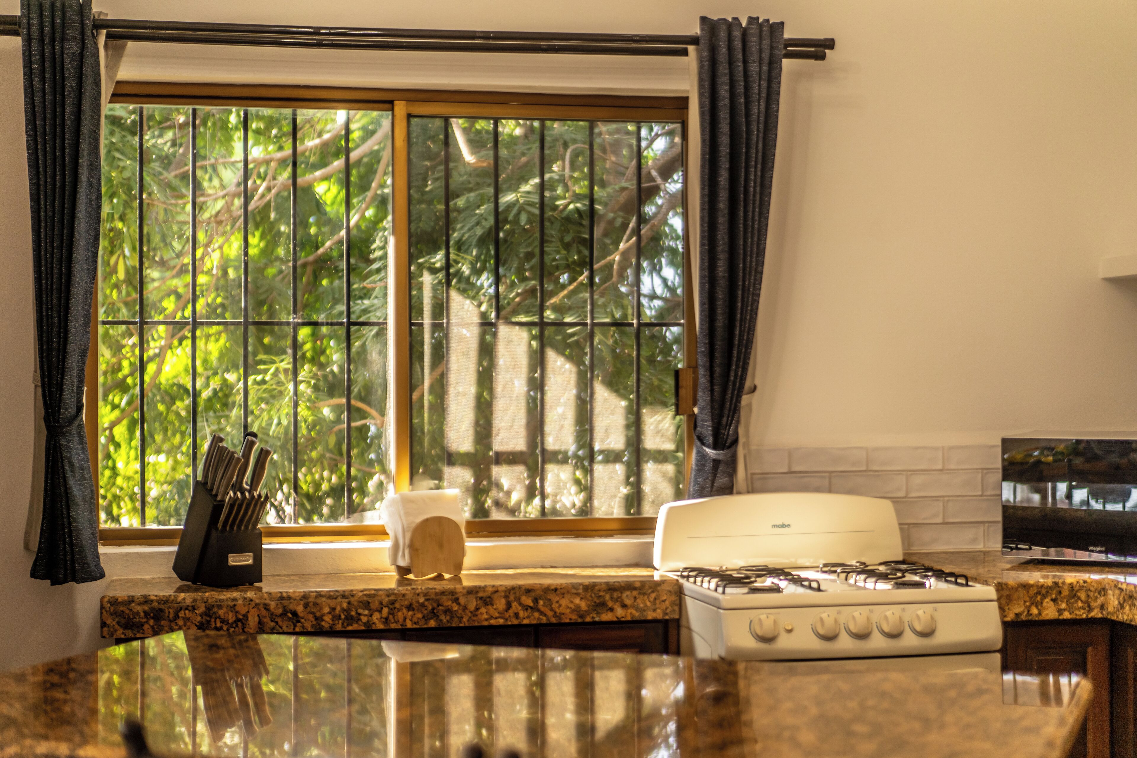 A kitchen with a stove, a window with curtains, and a knife block on the counter.