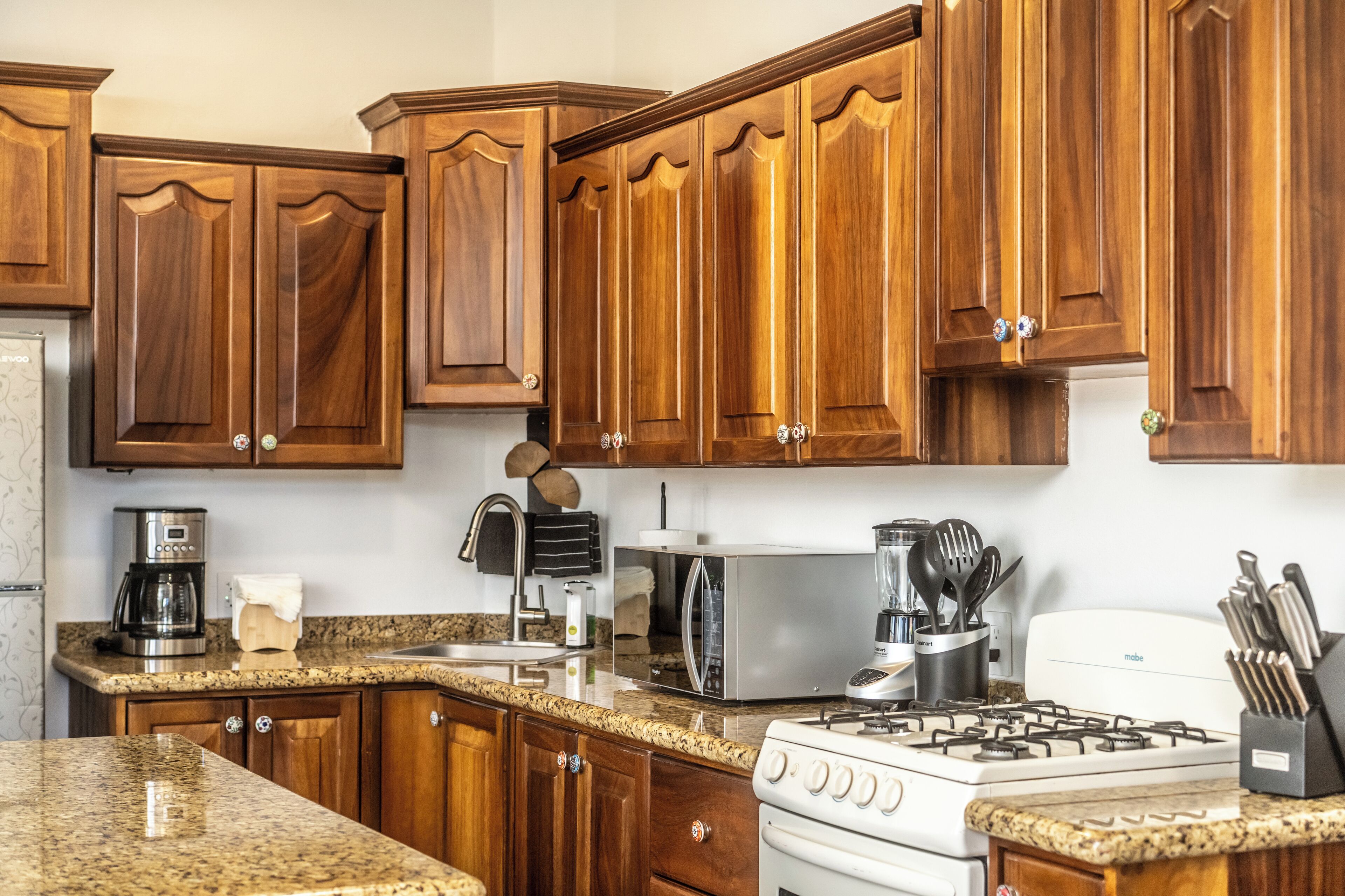 A kitchen with wooden cabinets, granite countertops, a stove, a microwave, and various appliances.
