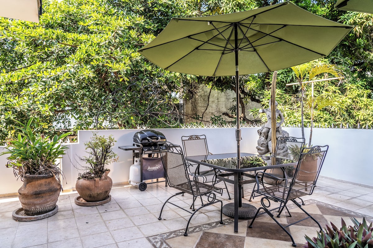 Eine Terrasse im Freien mit Tisch, Stühlen, einem Grill und Kübelpflanzen.