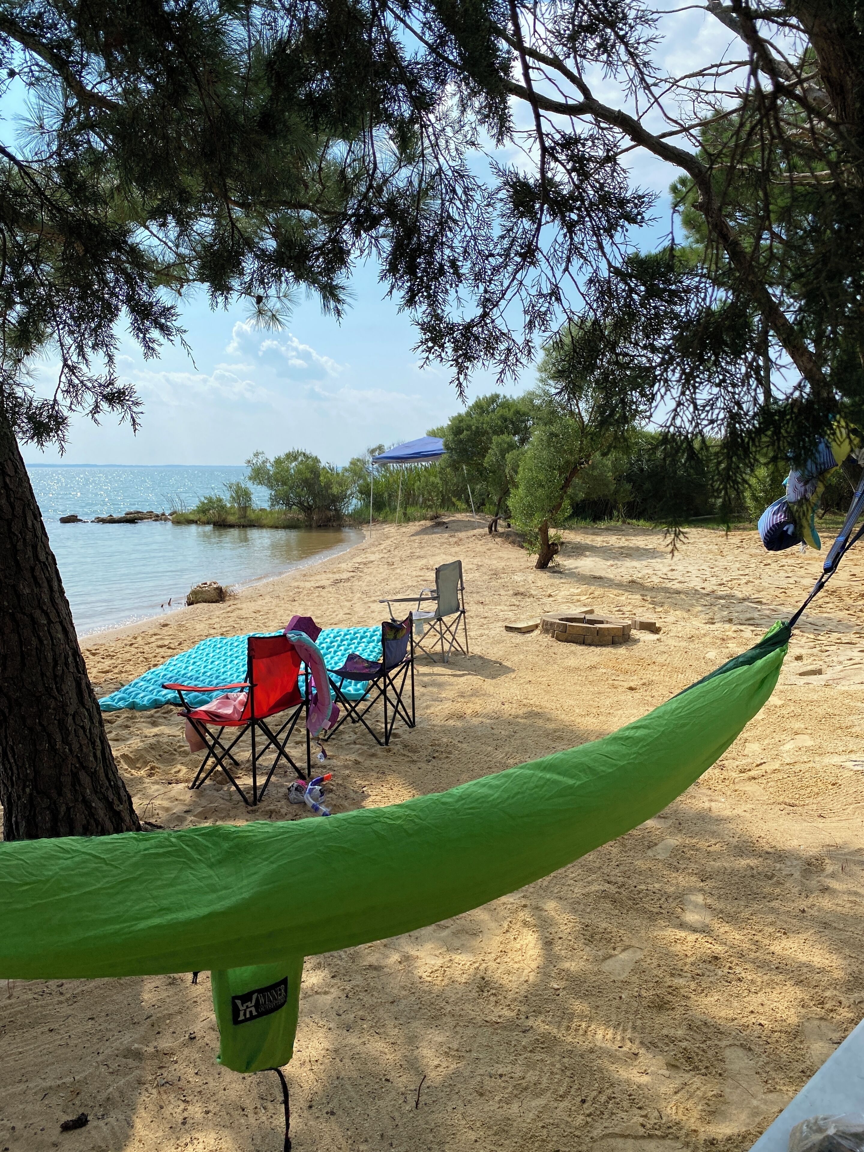 A beach with a hammock, a blue beach umbrella, and a red chair.