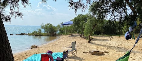 Una playa con una hamaca, una sombrilla azul y una silla roja.