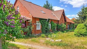A traditional brick house with a red-tiled roof, surrounded by lush greenery and flowering plants. - Ferienwohnung Klocksin (Klocksin)