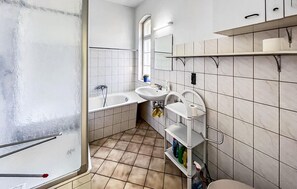 Uma casa de banho com banheira, duas pias, sanita e estantes.