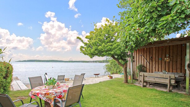 Une terrasse avec une table et des chaises, une plateforme en bois et une vue sur un lac.