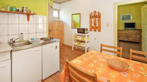 Una cocina compacta con estufa, pileta y muebles bajos de madera. Se observa una mesa de comedor con sillas y un televisor al fondo.