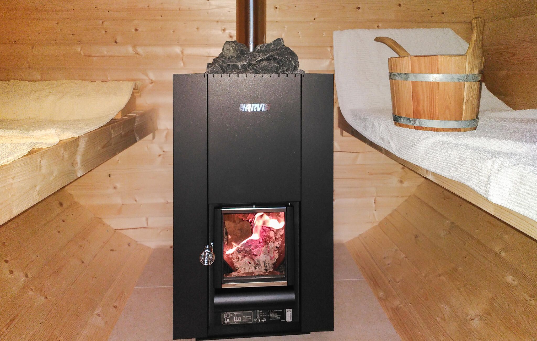 A wood-burning stove with a visible fire, a metal container, and a wooden bench.