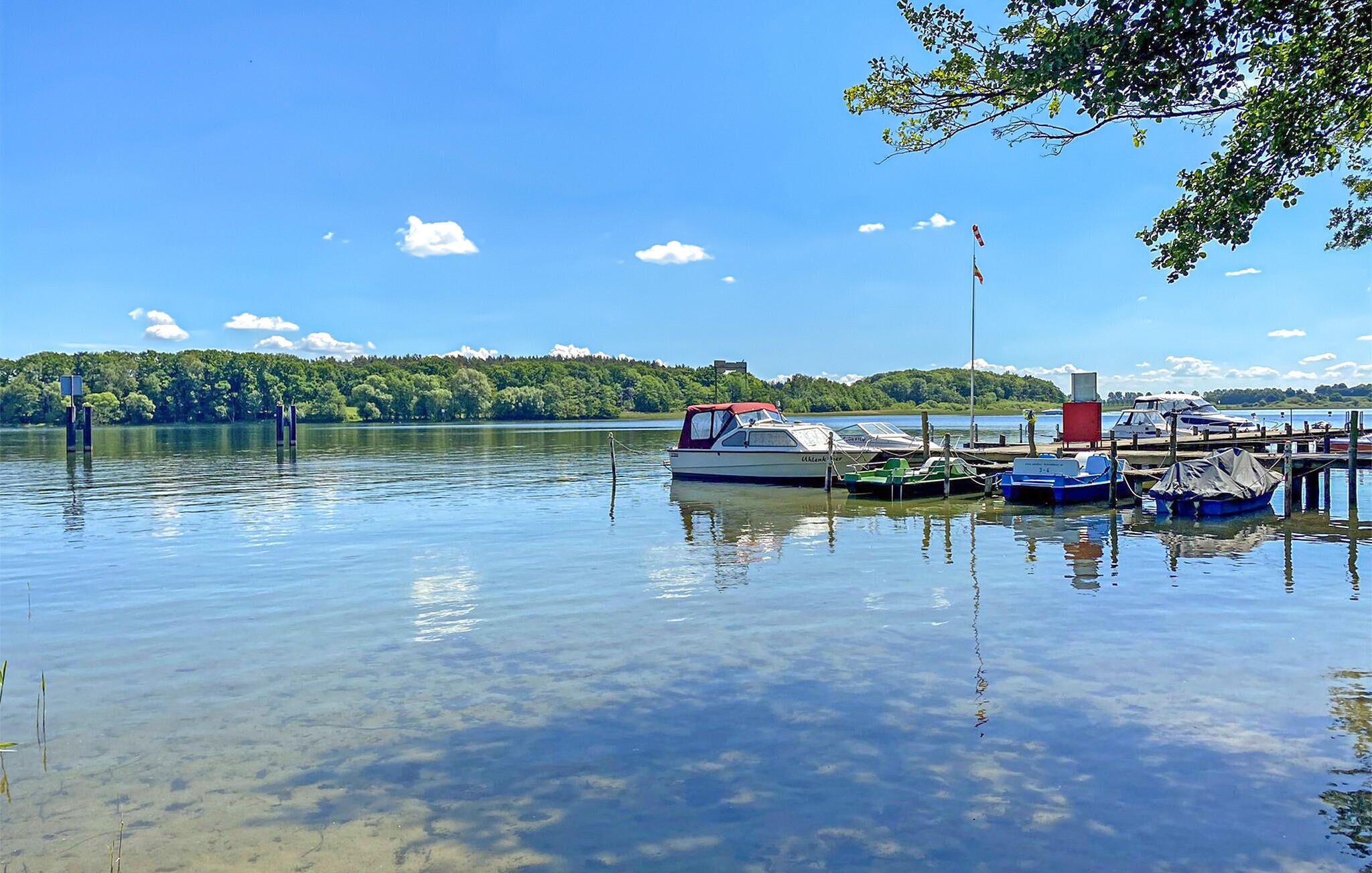 Un lago tranquilo con barcos amarrados en un muelle, rodeado de exuberante vegetación y un cielo despejado.