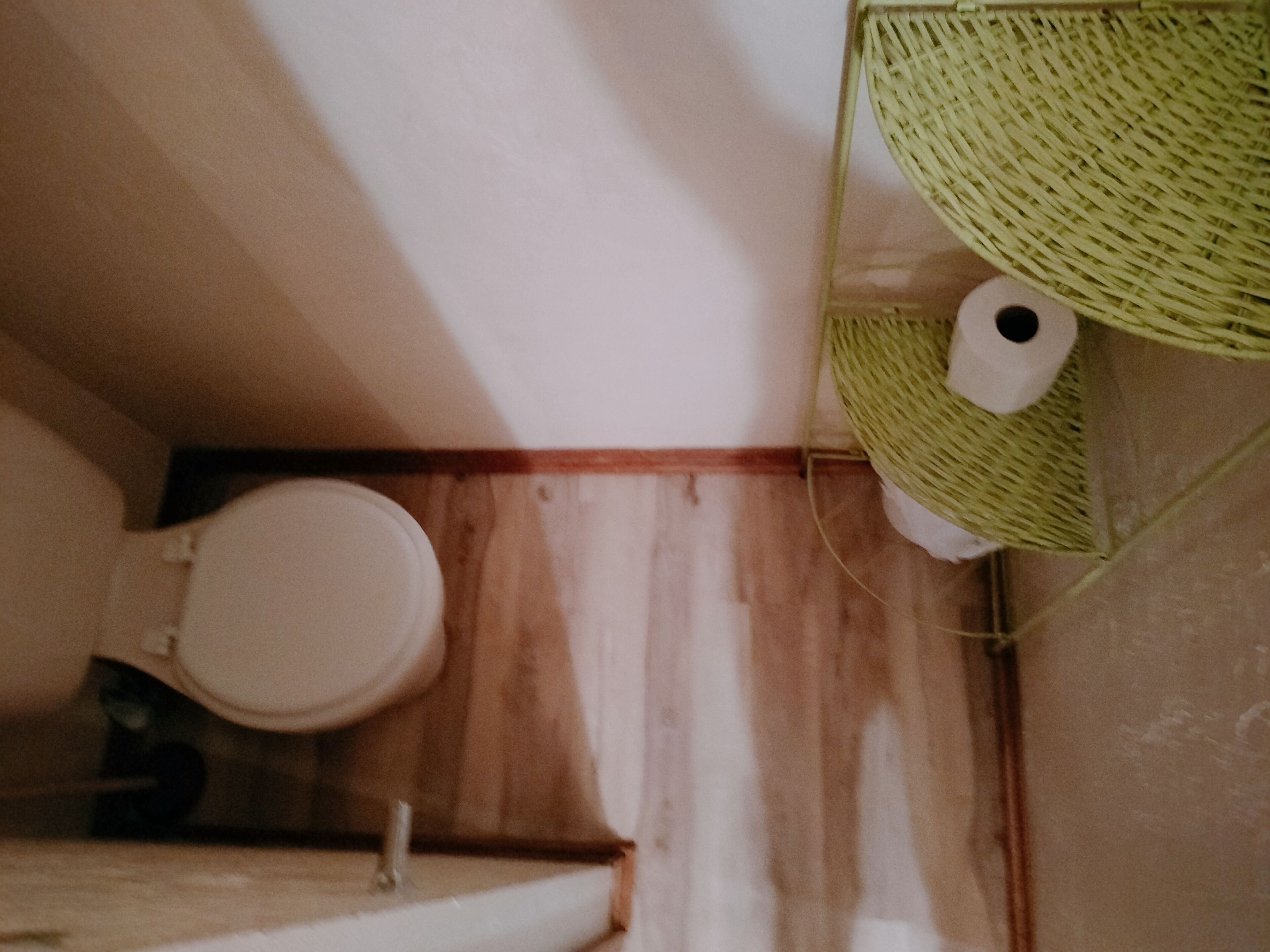 A bathroom with a wooden vanity, a toilet, and a green woven basket hanging on the wall.