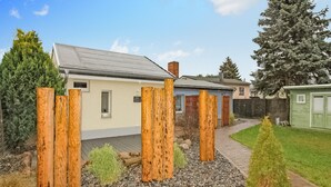 Une maison avec un toit gris, un petit garage attenant et une clôture en bois dans le jardin avant.