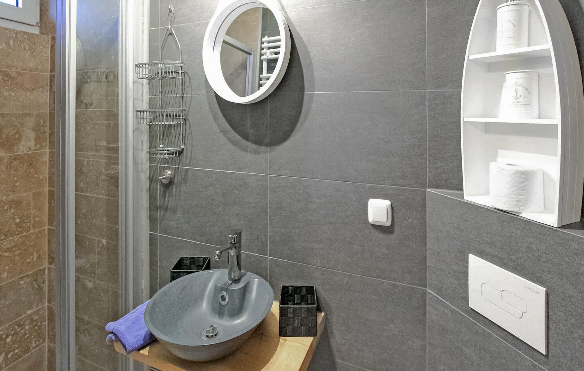 A modern bathroom with a round mirror, a vessel sink, a towel, and a shelf with toiletries.