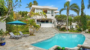 A modern house with a swimming pool, surrounded by lush greenery and palm trees.