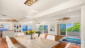 A modern dining area with a large table, white chairs, and a vase of sunflowers.