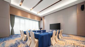 A conference room with a long table, beige chairs, a large screen, and a patterned carpet.