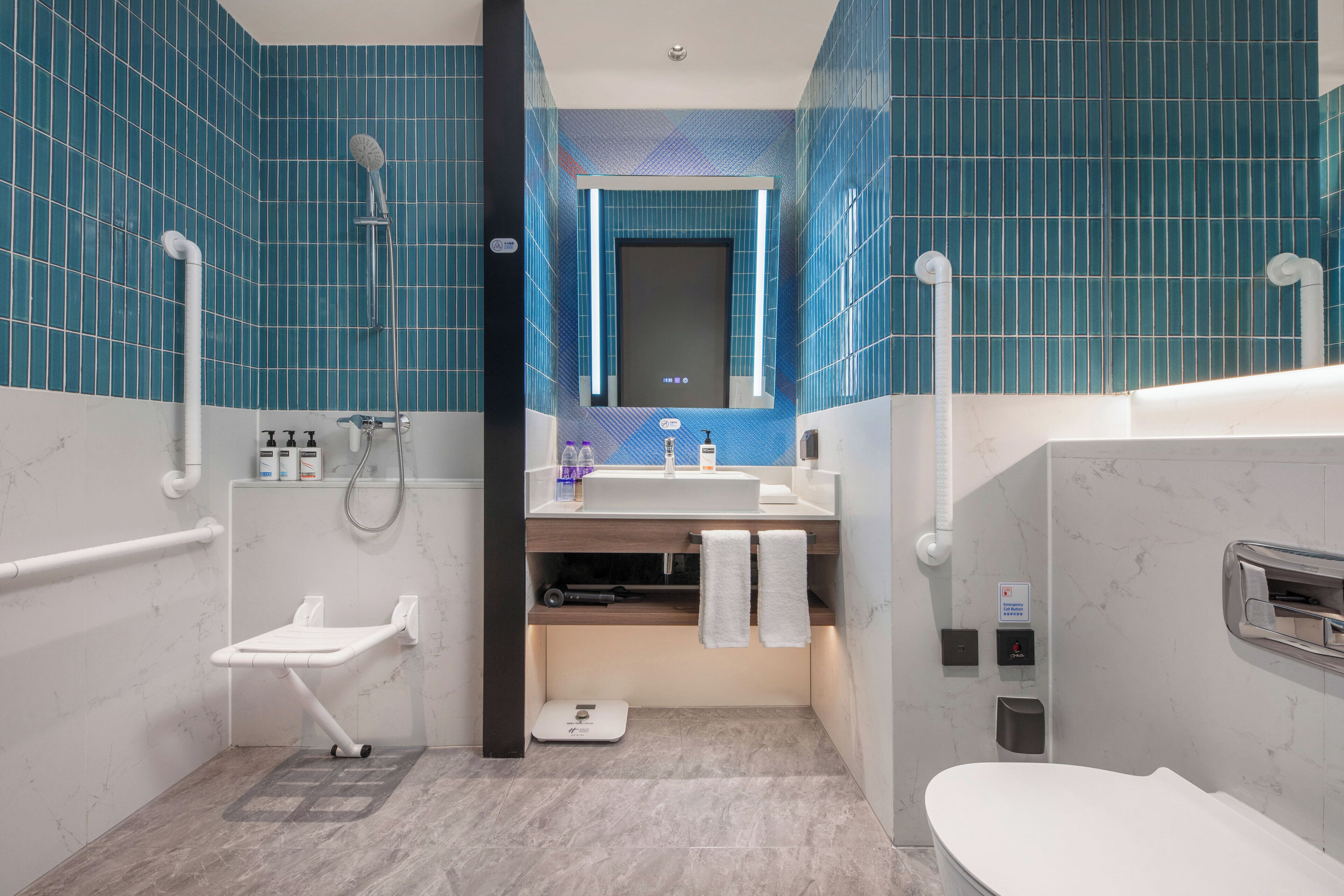 A modern bathroom with blue tiles, a white sink, a mirror, a shower, and a toilet.