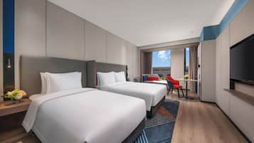 Habitación de hotel con dos camas, televisión, escritorio y vista al exterior.