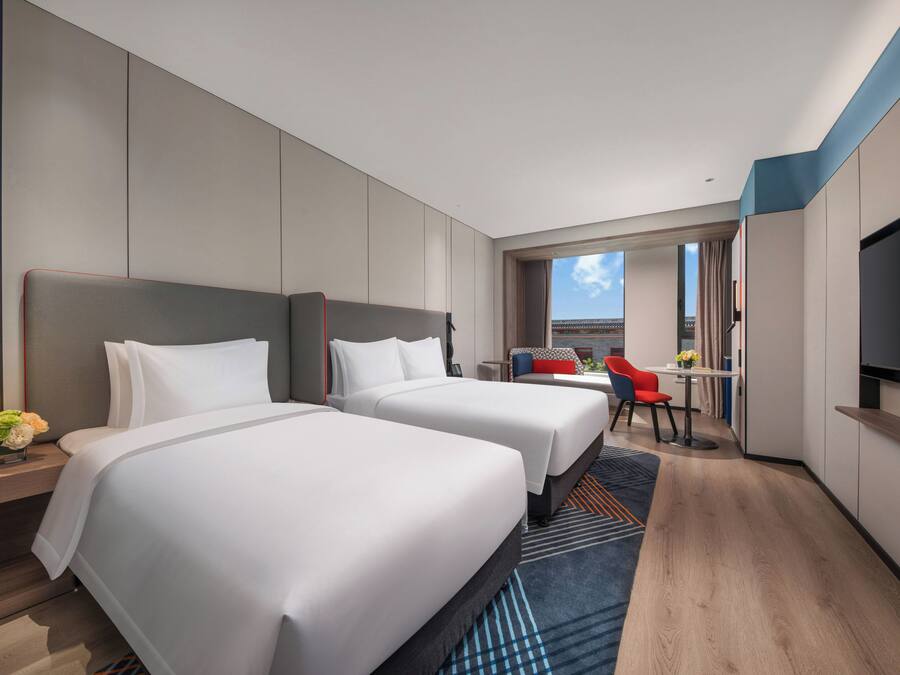 Habitación de hotel con dos camas, televisión, escritorio y vista al exterior.