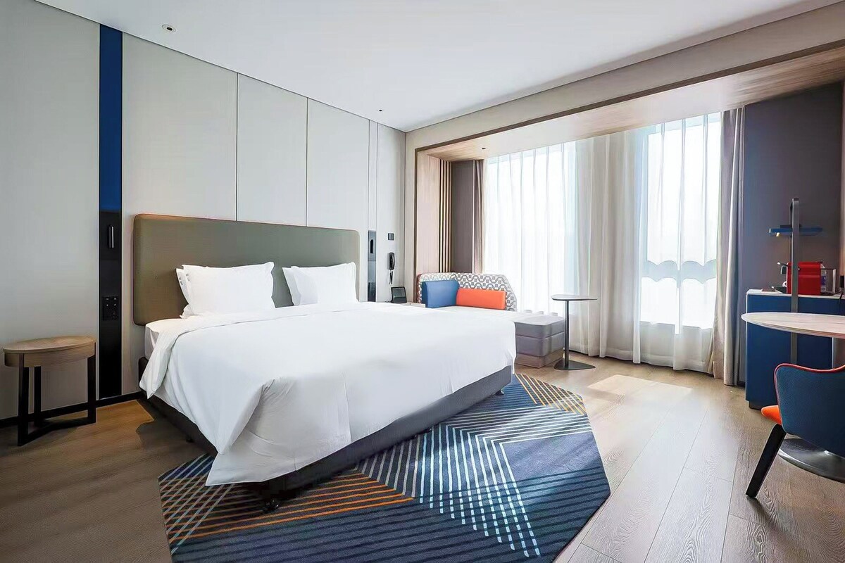 A modern hotel room with a large bed, a desk, and a chair.