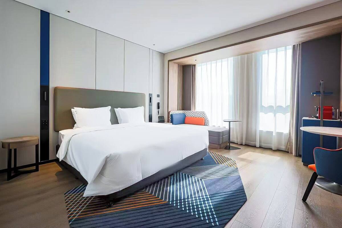 A modern hotel room with a large bed, a desk, and a chair.