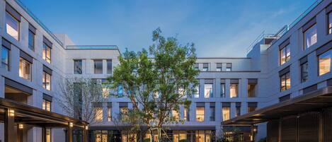 Un bâtiment moderne à plusieurs étages, doté de grandes fenêtres et d’une cour intérieure agrémentée d’un arbre et de verdure.