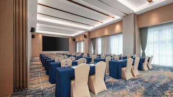 A conference room with rows of tables and chairs, a large screen, and a carpeted floor.