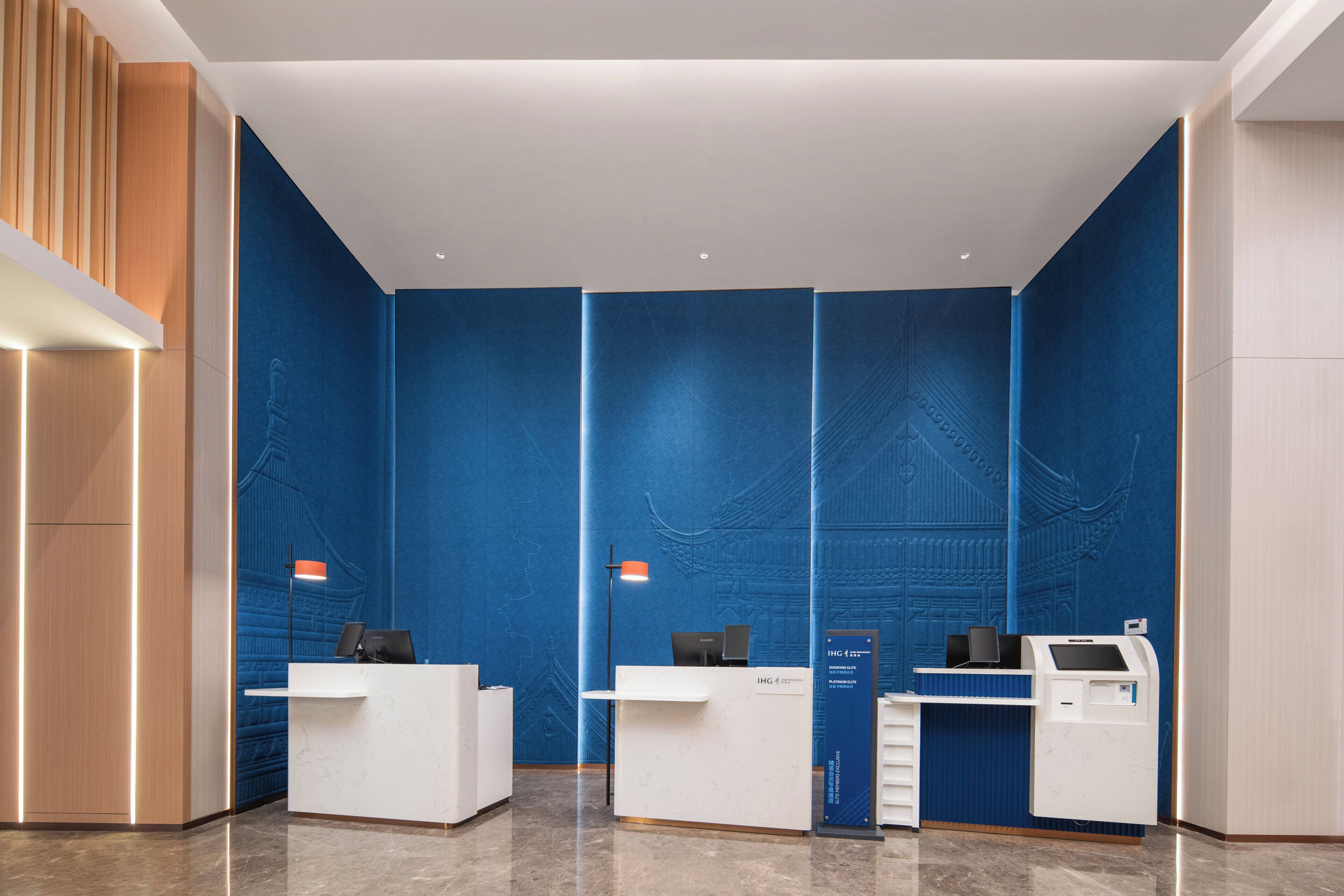Ein Empfangsbereich mit zwei weißen Empfangstheken, einer blauen Wand mit Struktur und einem modernen Design.