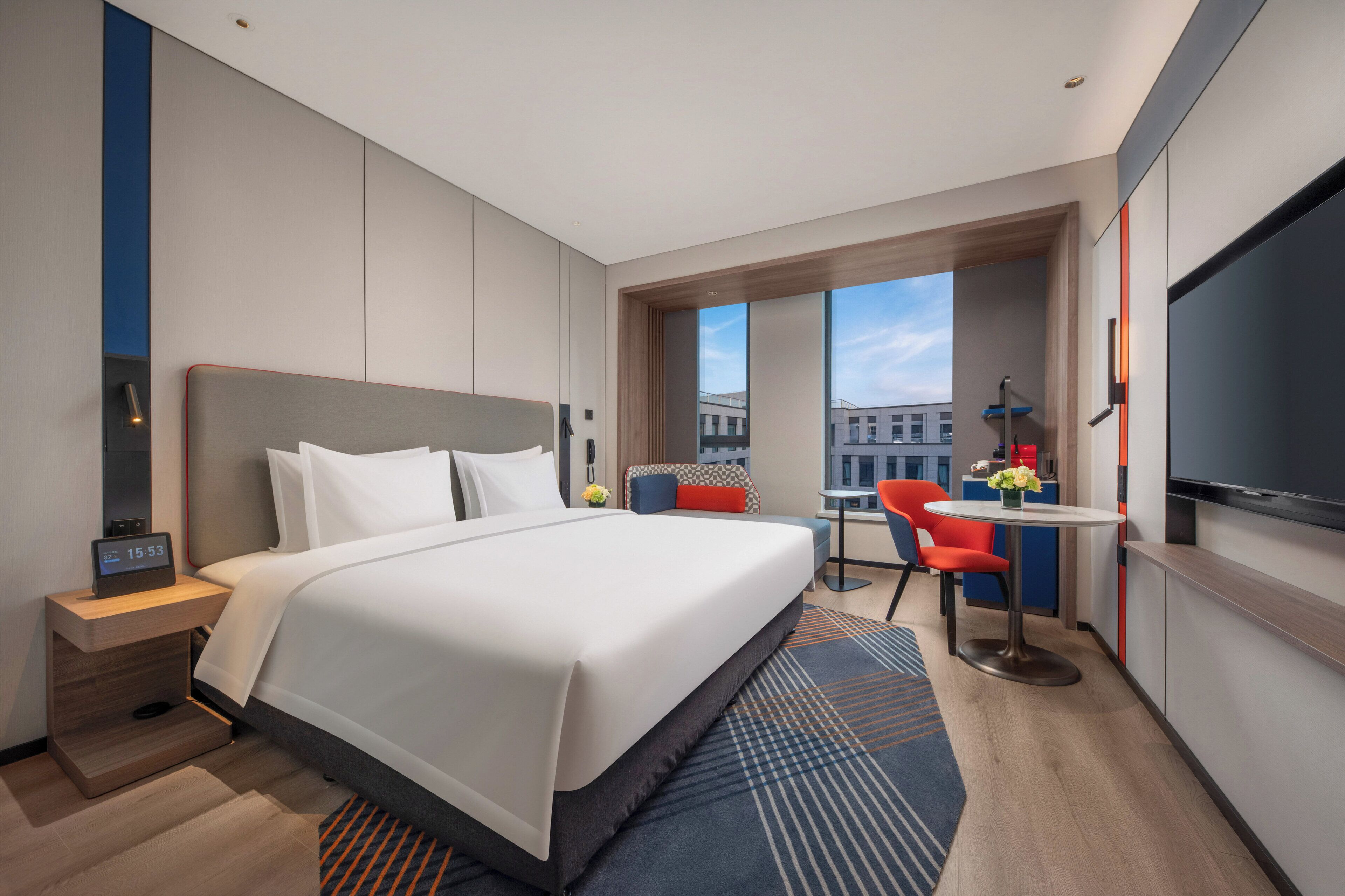 Una habitación de hotel moderna con una cama grande, un escritorio con silla, un televisor y una ventana con vistas a la ciudad.
