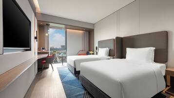 A hotel room with two beds, a desk, a TV, and a view of the city.