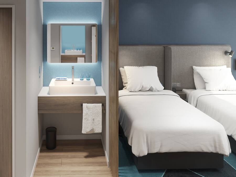 A modern hotel room with a wooden door, a bathroom with a sink and mirror, and two beds with white bedding.