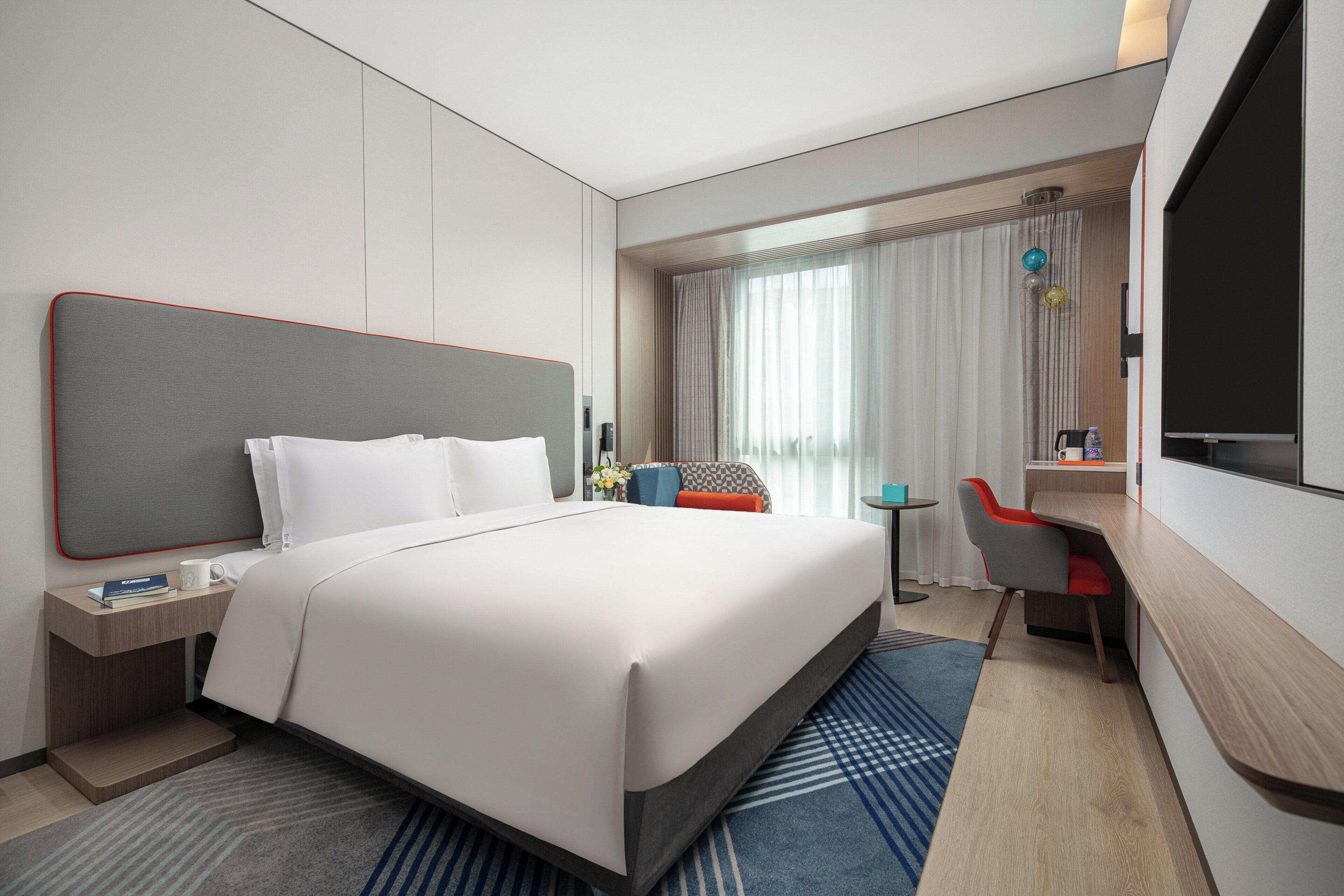Une chambre d’hôtel moderne, dotée d’un grand lit, d’un bureau, d’une chaise, d’une télévision et d’une fenêtre avec des rideaux.