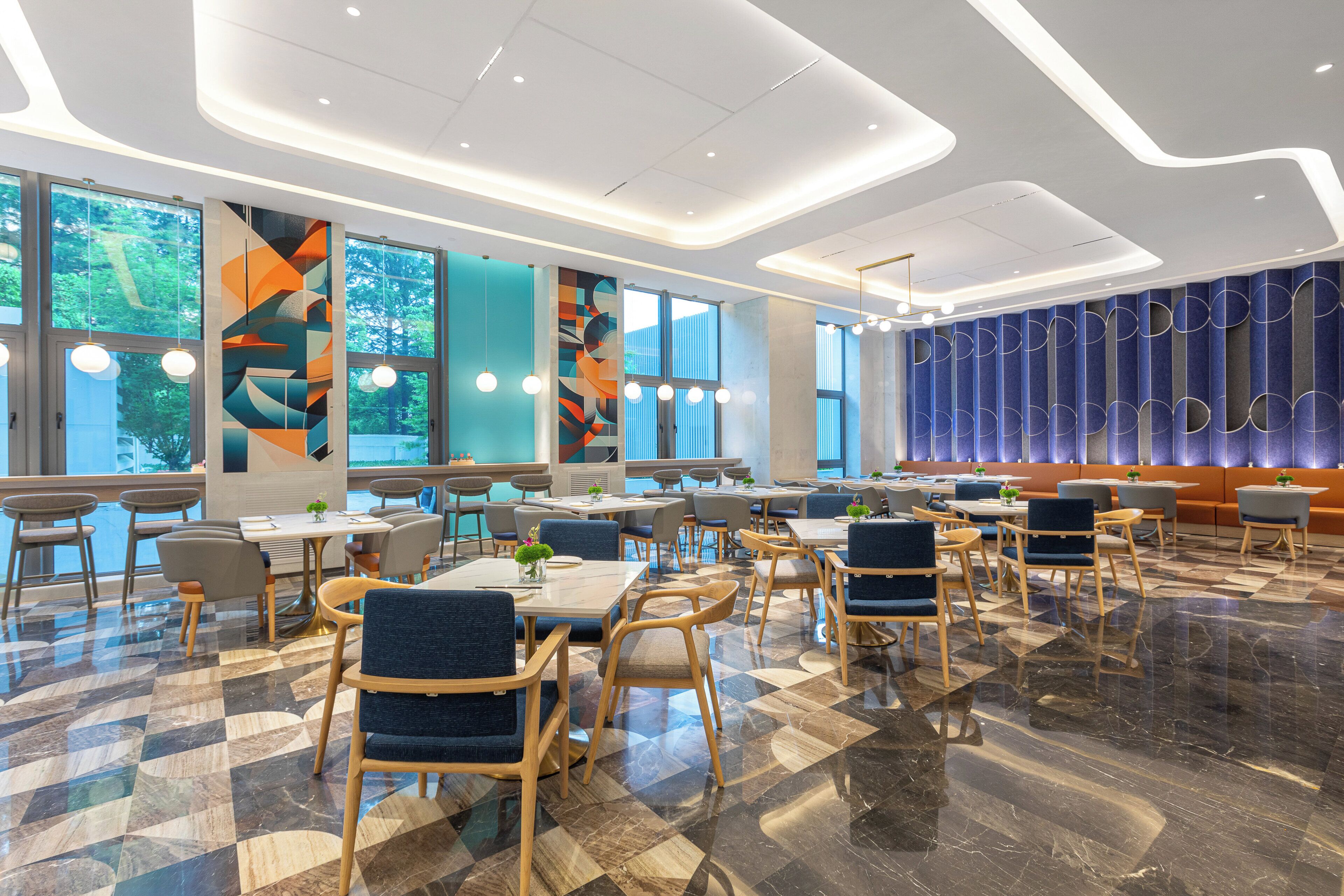 A modern dining area with a checkered floor, tables with chairs, and large windows offering views of greenery.