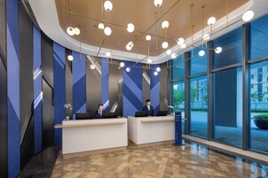 Un'area reception moderna con due scrivanie, un'ampia finestra che si affaccia sulla strada e un muro con motivo geometrico.