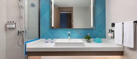 Un baño moderno con un espejo grande, lavamanos blanco y zona de ducha.