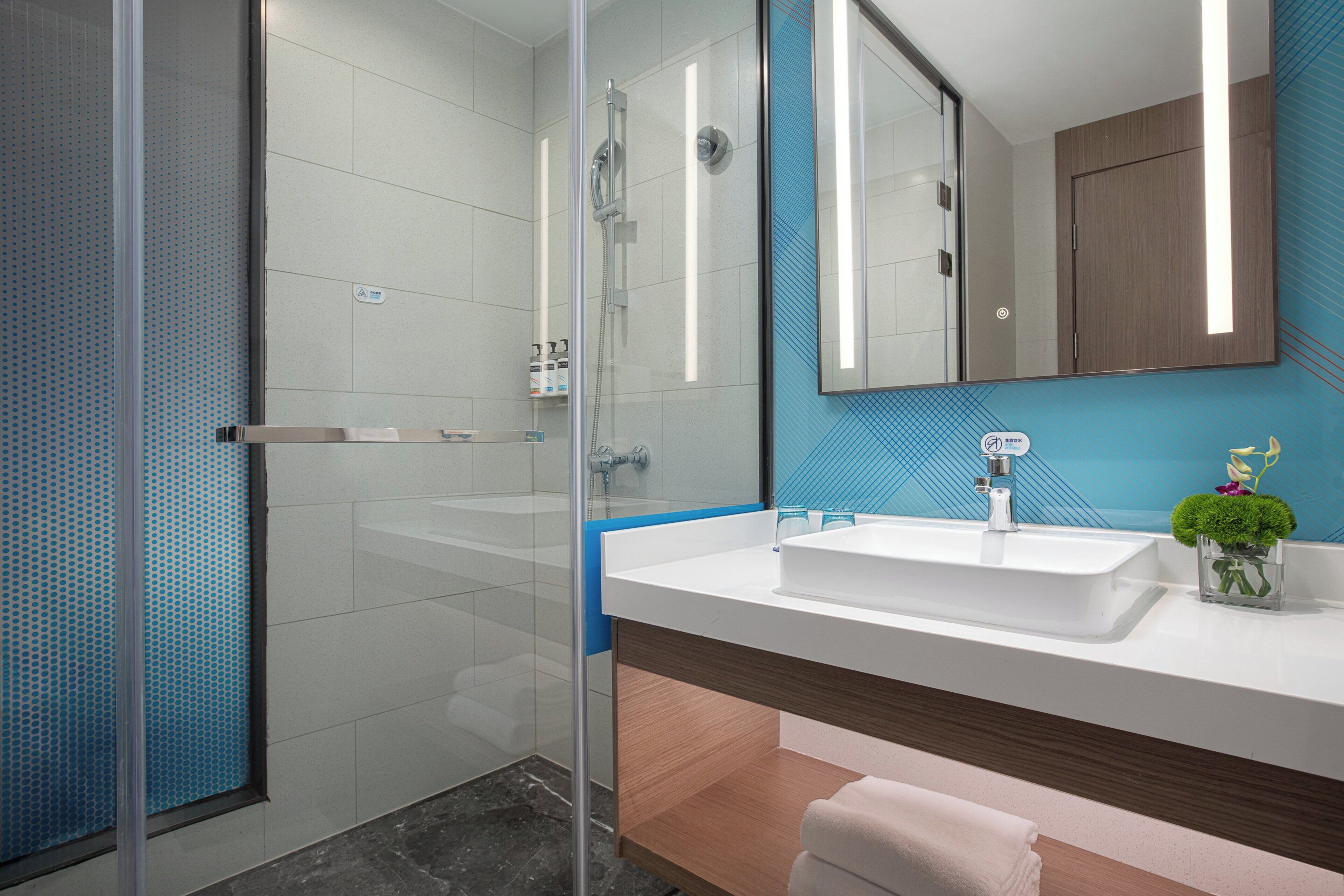 A modern bathroom with a glass shower enclosure, a white sink, and a blue tiled wall.