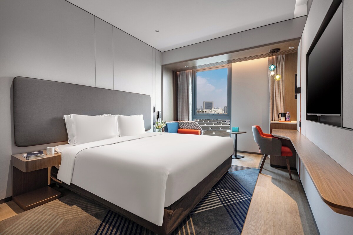 A modern hotel room with a large bed, a desk, and a TV.