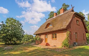 Ett traditionellt hus byggt av tegel med ett halmtak, en skorsten och en liten veranda.