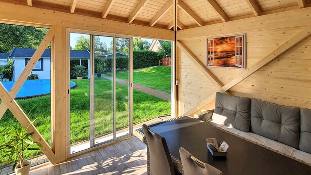 A cozy wooden interior with a dining area, a sofa, and a view of a green garden and neighboring houses. - Ferienwohnung Neppermin/Usedom (Neppermin/Usedom)