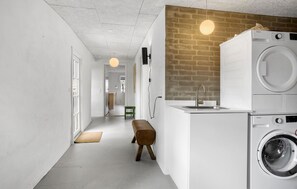 Laundry room with a front-loading washer and dryer, a brick accent wall, and a wooden bench for seating.