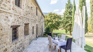 A stone building with a patio table set for dining, surrounded by greenery and trees. - Il Casale di John - Discover Authentic Italy (Umbertide)