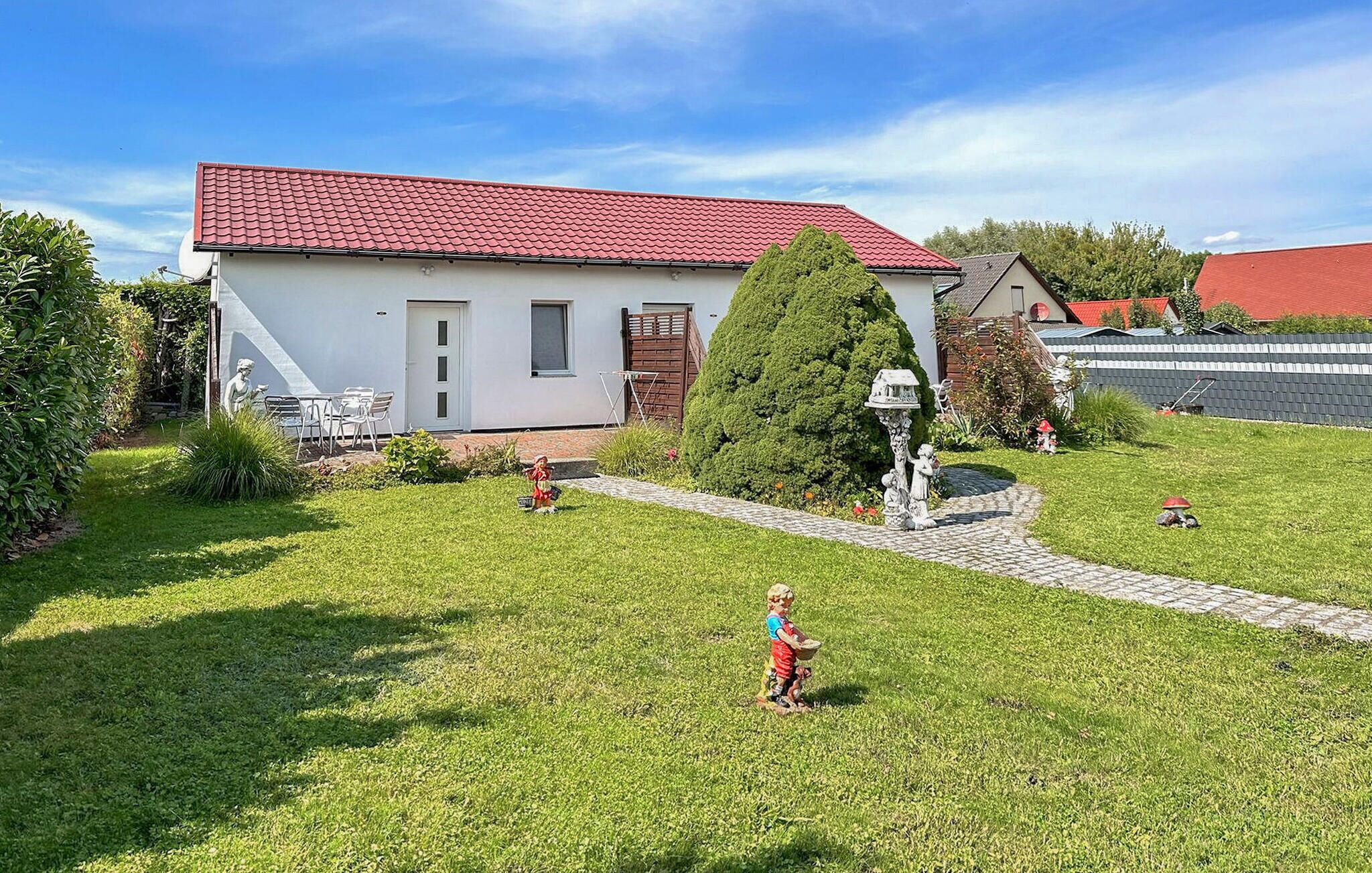 Une maison avec un toit recouvert de tuiles rouges, un petit jardin avec un chemin pavé et une statue au centre.