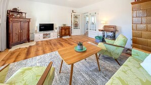 A living room with wooden flooring, a TV, a cabinet, a sofa, and a chair.