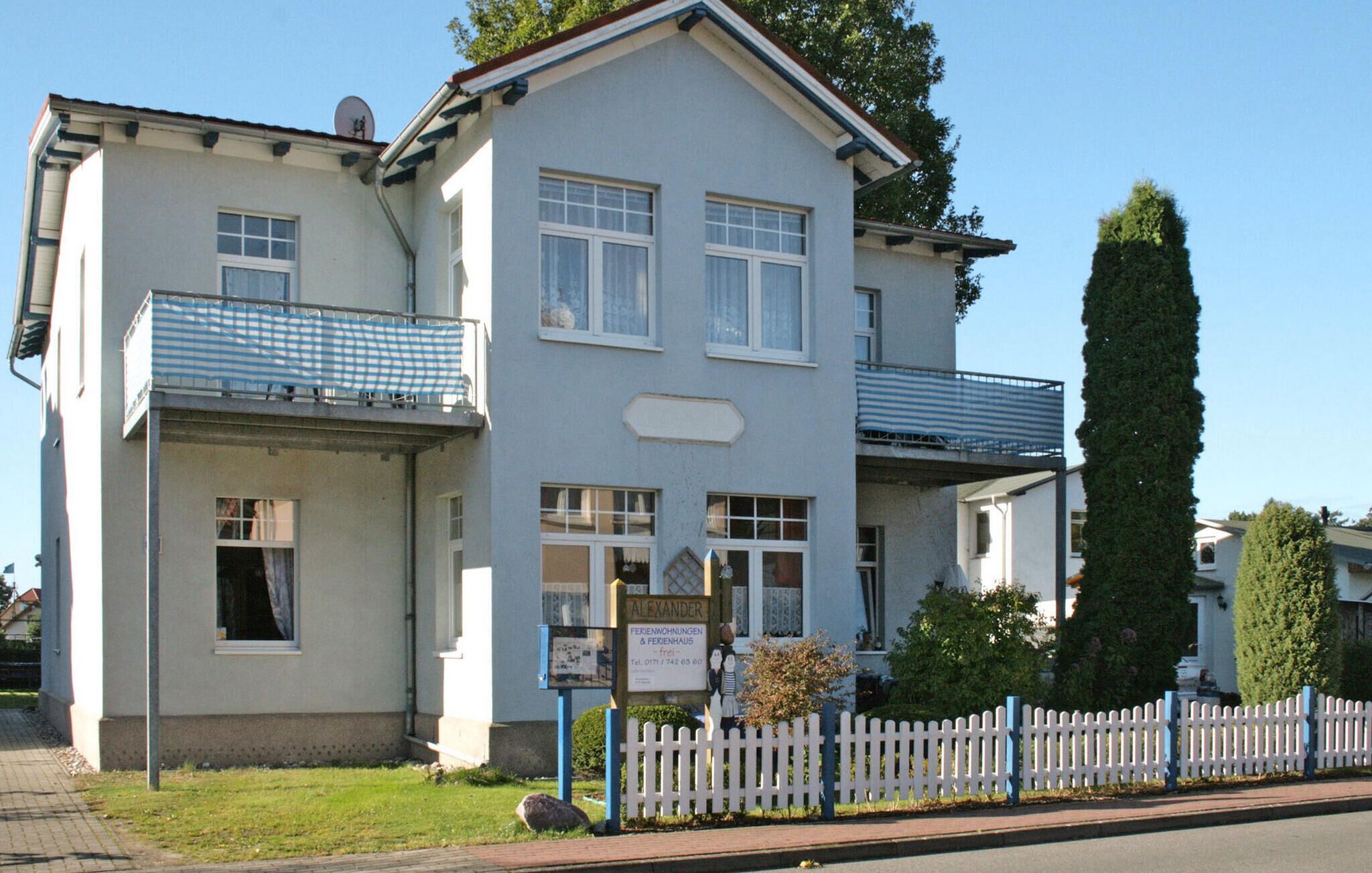 A two-story building with a balcony, a signboard, and a white picket fence.