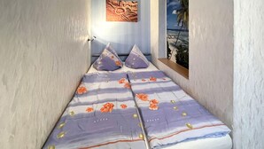 Pieni, kapea huone, jossa on sänky, jonka päällä on kukkakuviollinen päiväpeite ja kaksi tyynyä.
