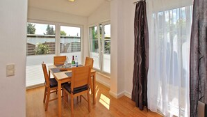 Un comedor con mesa y sillas, ventanas grandes con persianas y vistas al exterior.