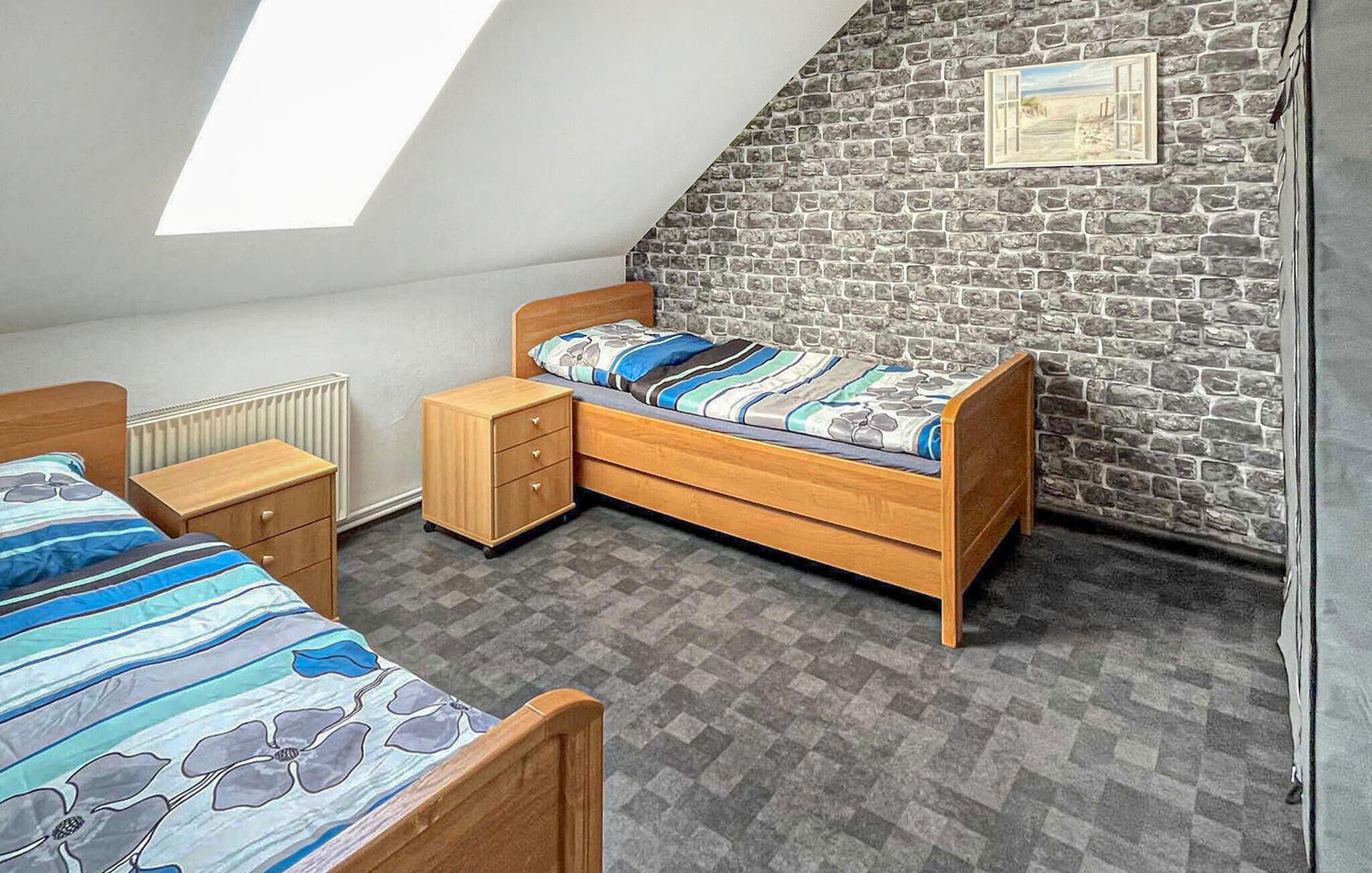 Un dormitorio con techo inclinado, cama de madera, mesita de noche, cómoda y pared de piedra con un cuadro.