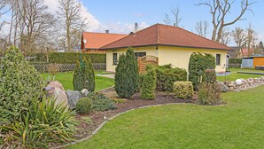 Ein gelbes Haus mit rotem Dach, umgeben von gepflegten Gärten und Hecken.