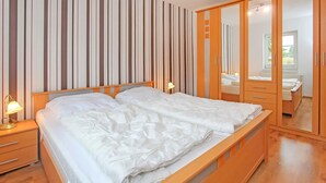 Ein ordentlich bezogenes Bett mit weißen Leinentüchern in einem Zimmer mit Holzmöbeln und einer gestreiften Wand.
